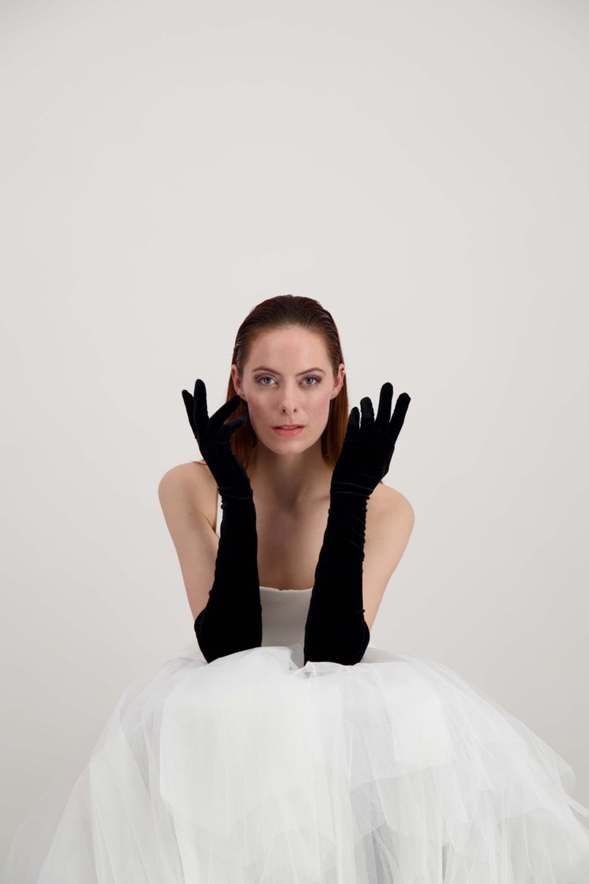 Jeune femme rousse, les mains aux oreilles, habillée d'une robe blanche et d'une paire de gants en velours noir